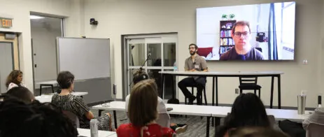 Max Blau sits facing a group of MFA students as a screen in the background shows Jacob Feldman.