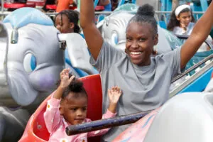 A mother and her child hold up their arms and smile as they ride an elephant ride at the fair.