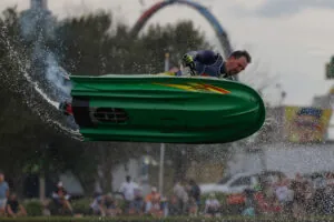 A boat jumps over water as water pellets fly around at the fair.