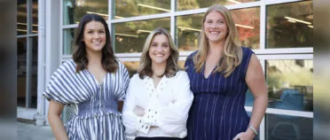 Three women pose for a portrait outside the Grady College building.