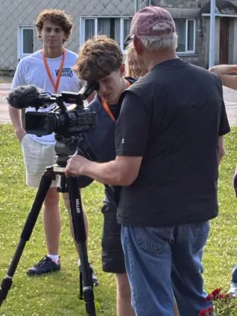 A student looks through the viewfinder of a film camera as others look on.