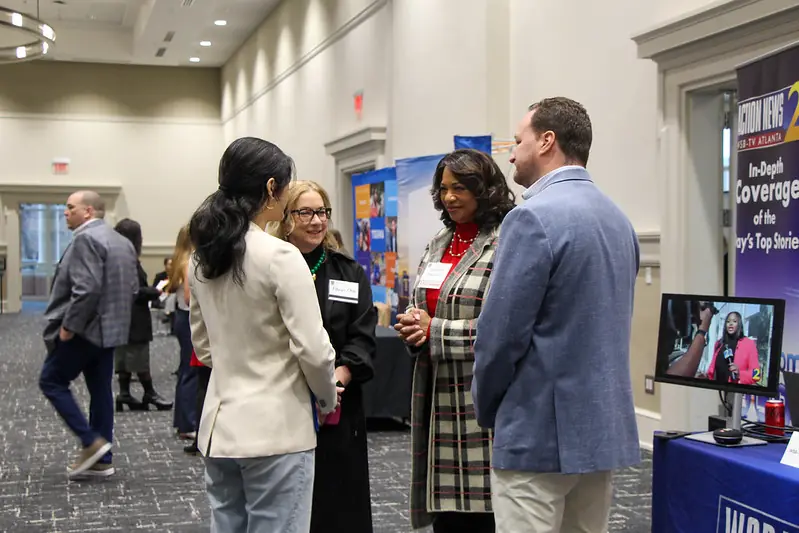 Group of professionals stand up and talk to one another during career fair.