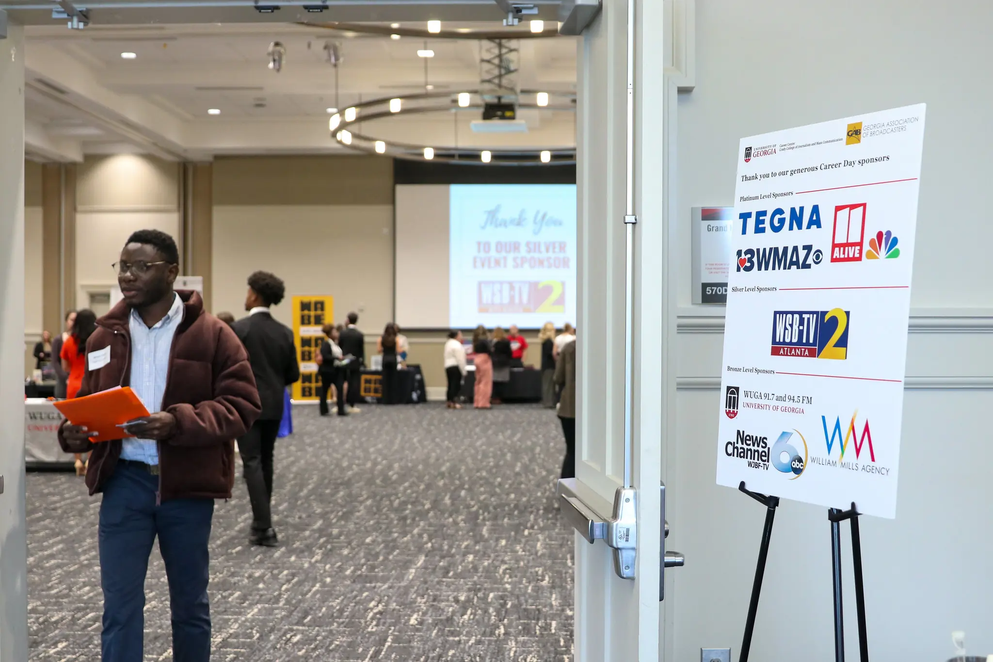 Student exits the career fair through doors. A sign with sponsor logos is on an easel to the right.