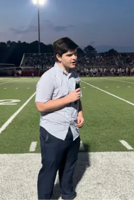 Picture of Peter Bartlett speaking in a microphone on a football field.