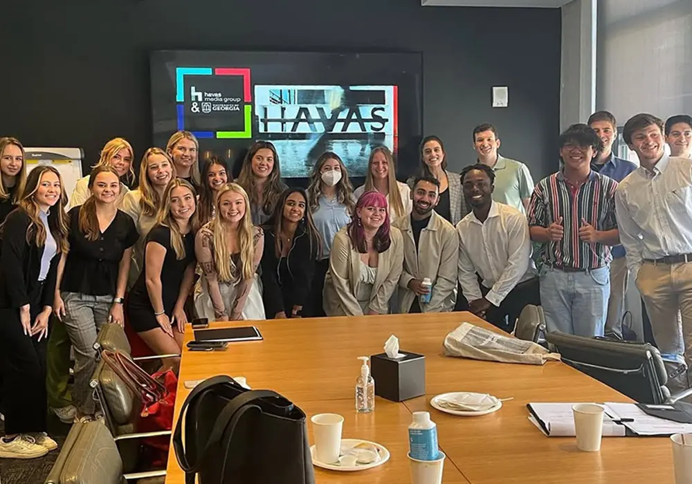 A group of students are pictured at the end of a conference table in an office.