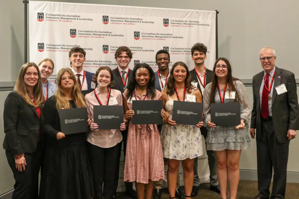 A group of students holding certificates pose for a picture in front of a step-and-repeat that says Cox Institute for Journalism, Innovation & Leadership, University of Georgia.