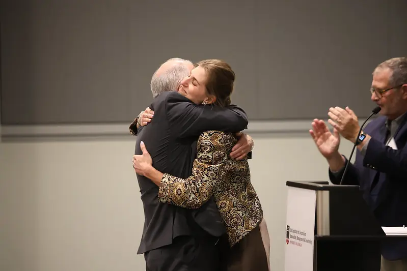 A man and woman hug in front of a podium.