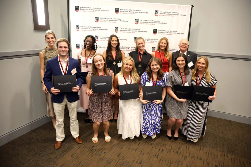 A group of students holding certificates pose for a picture in front of a step-and-repeat that says Cox Institute for Journalism, Innovation & Leadership, University of Georgia.