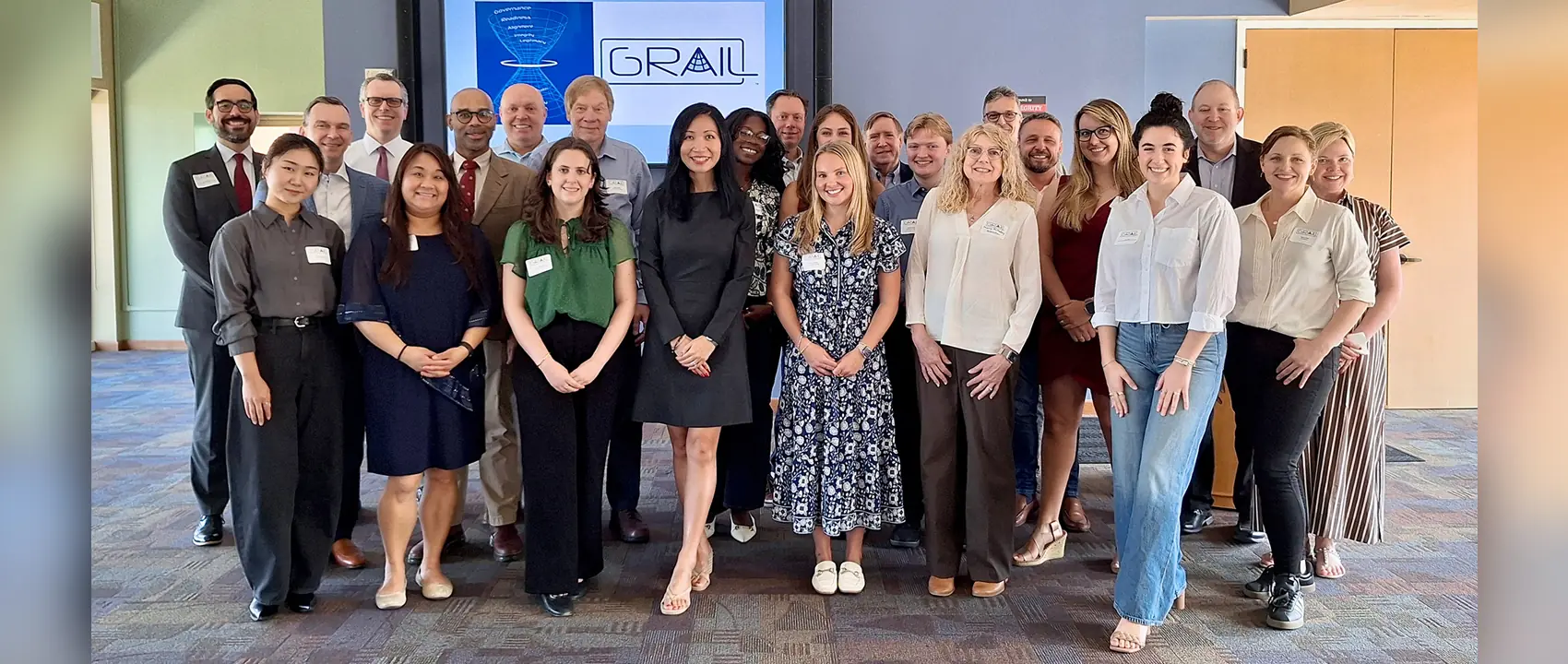 A group of people pose for a picture in front of a GRAIL digital sign.
