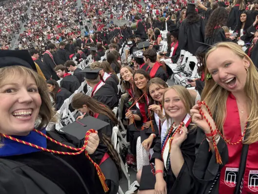 Several students and a faculty member who off their cords in a large graduation crowd.