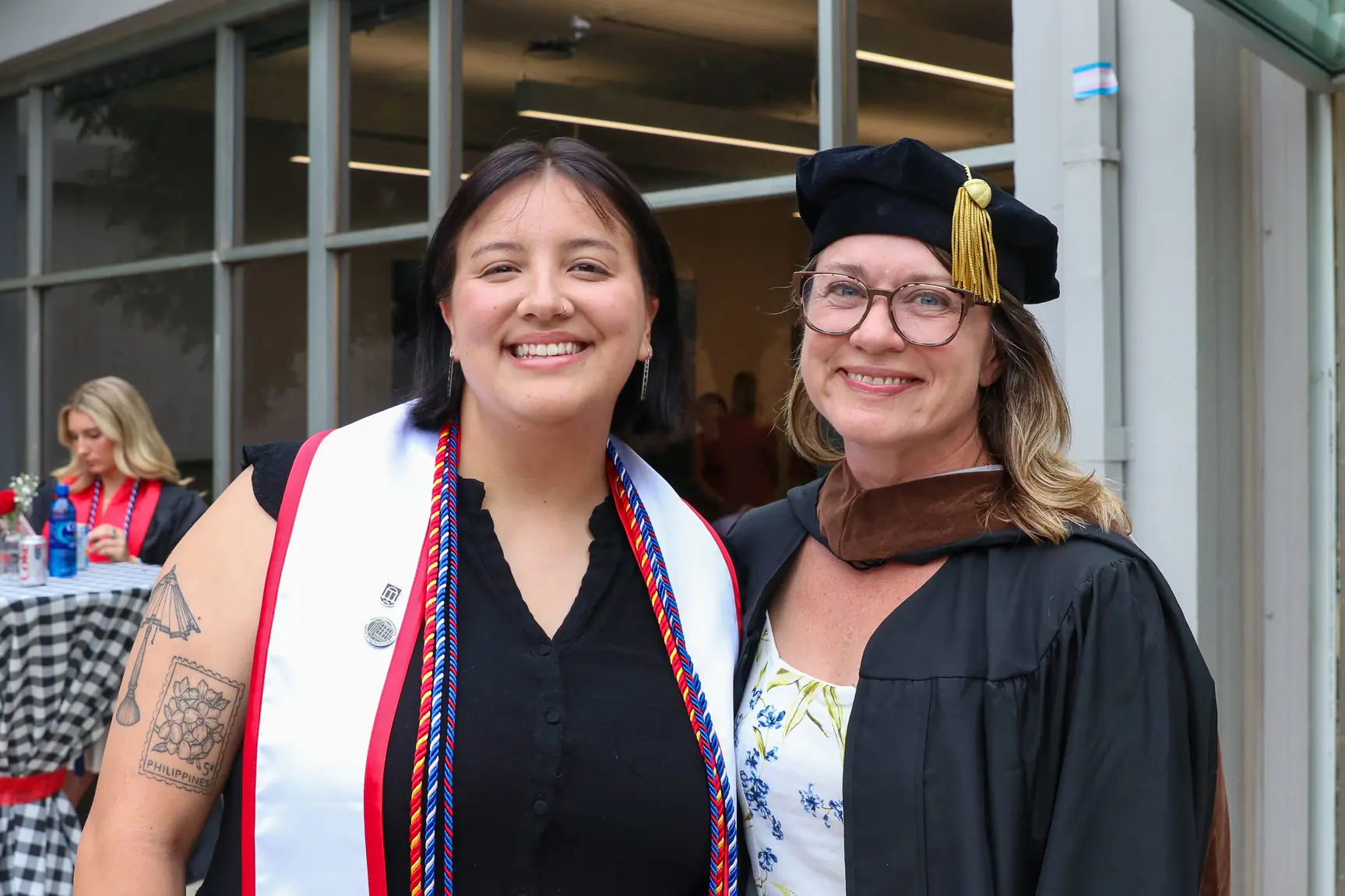 A graduate where a stole and cords poses for a picture with a faculty member outside of Grady College.