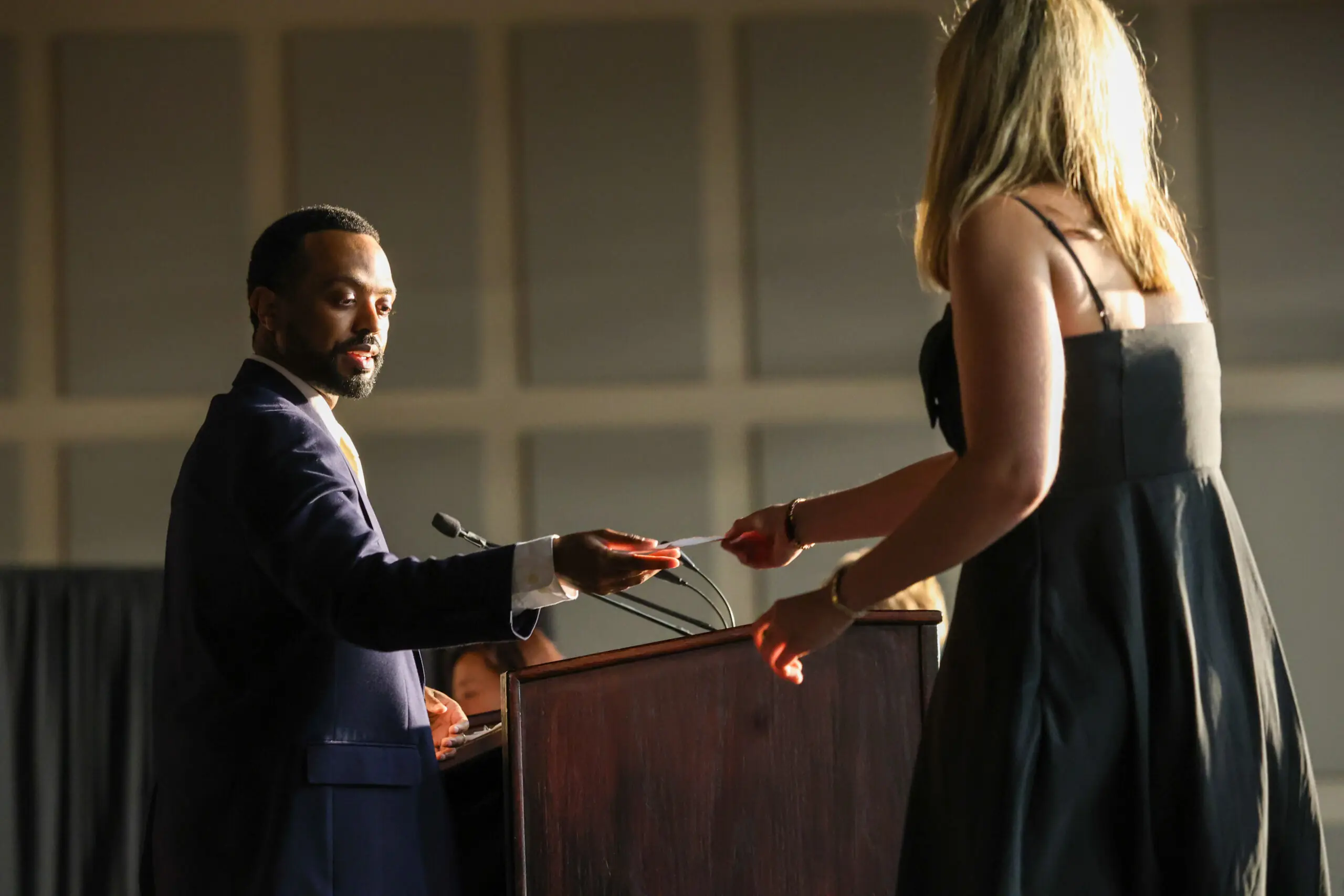 A man standing behind a podium receives something from a blonde young woman.