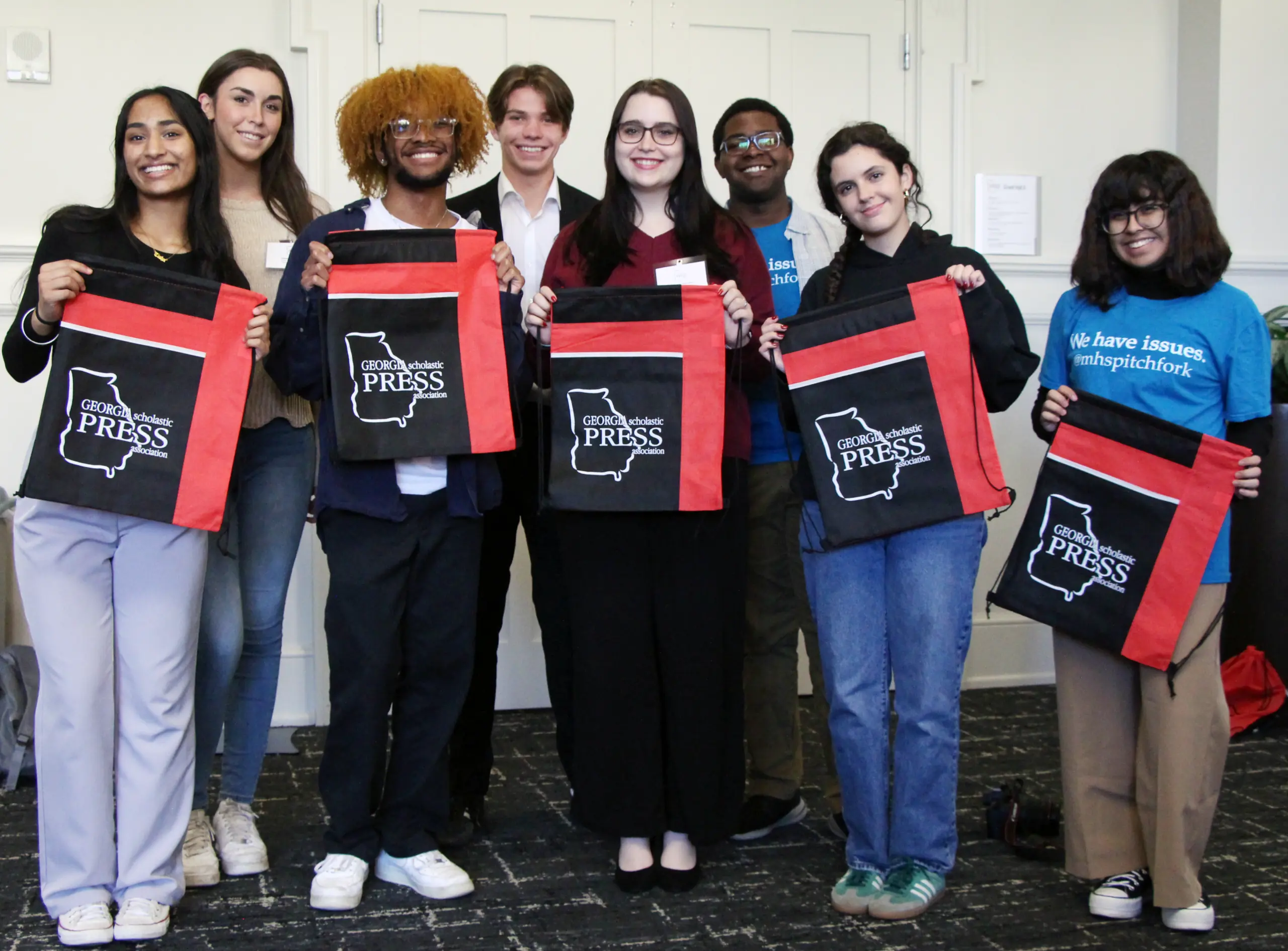 Eight students stand to pose for a picture holding tote bags that read "Georgia Scholastic Press Association."