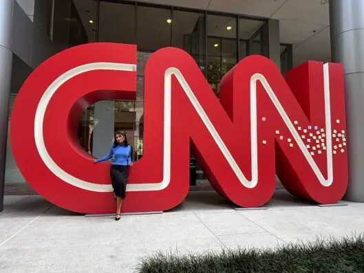 Full-body picture of Sanjana Copu standing in front of a CNN sign at an office building.