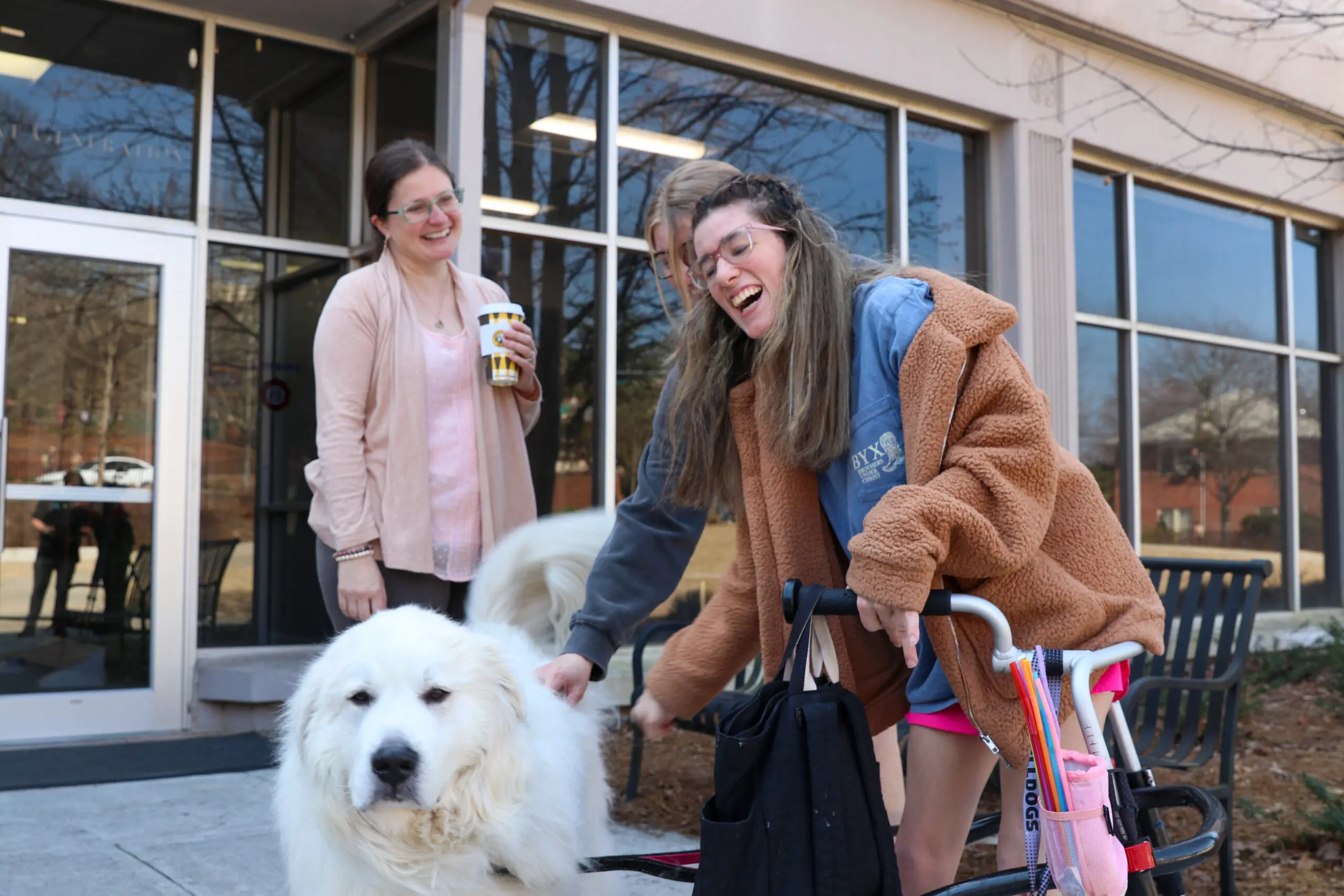 Three women stand next to a dog, petting it. The girl in the foreground has a medical walker.