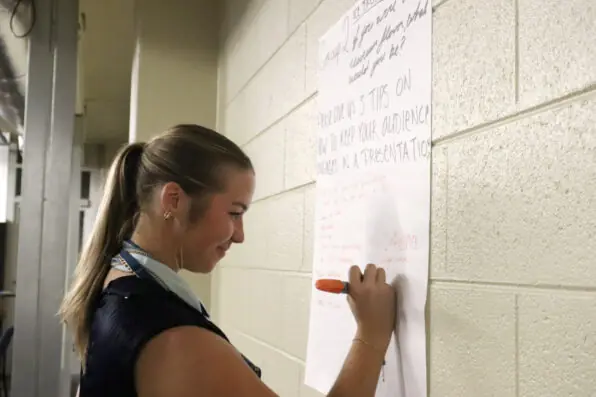 A female student writes on a large piece of paper hanging on the wall.