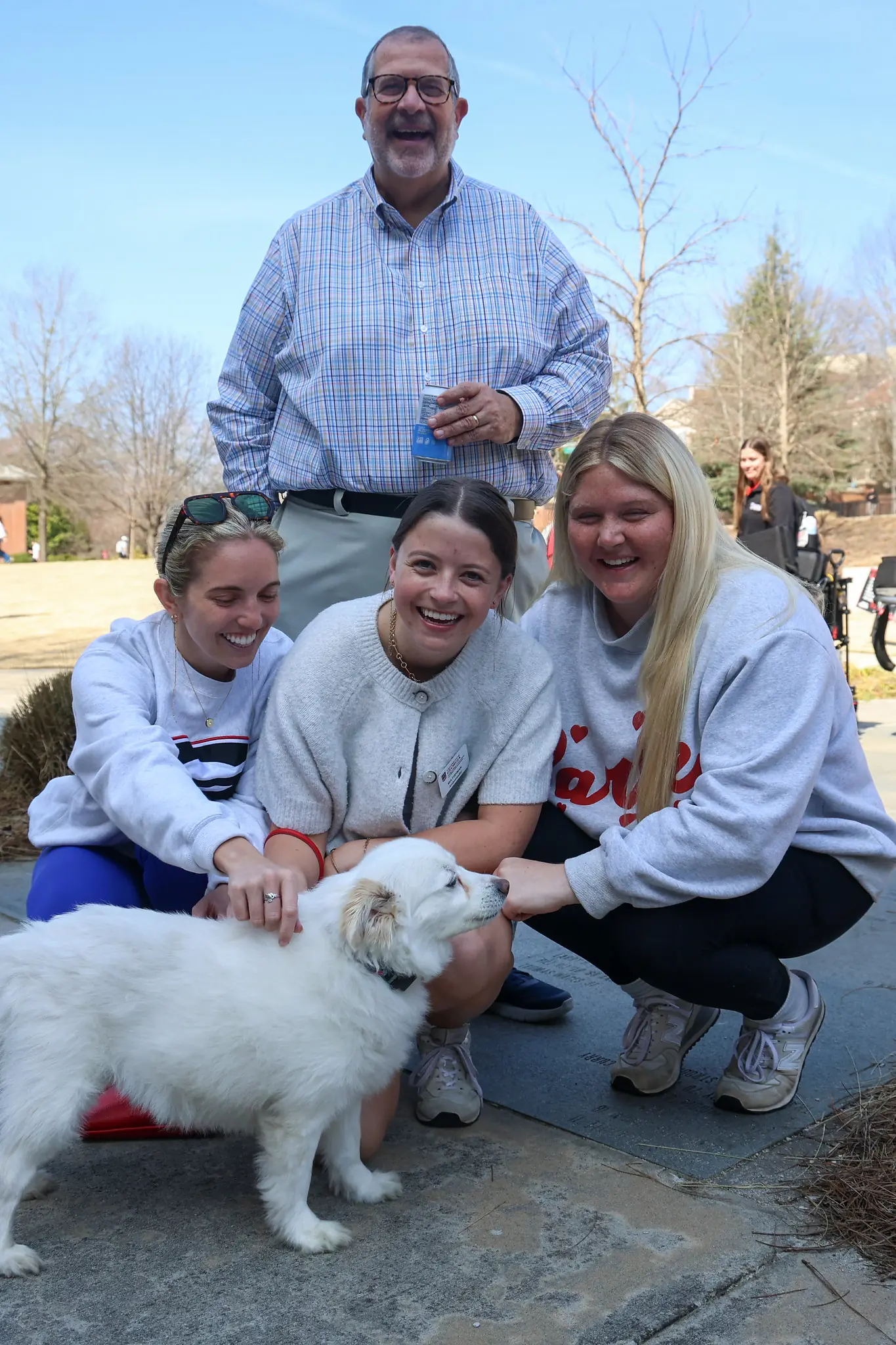 A man stands over three young women as they pet a white dog.