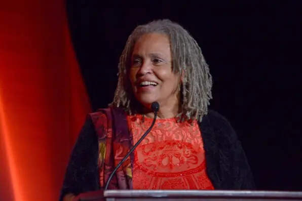 An older woman stands on stage in front of a microphone and podium.