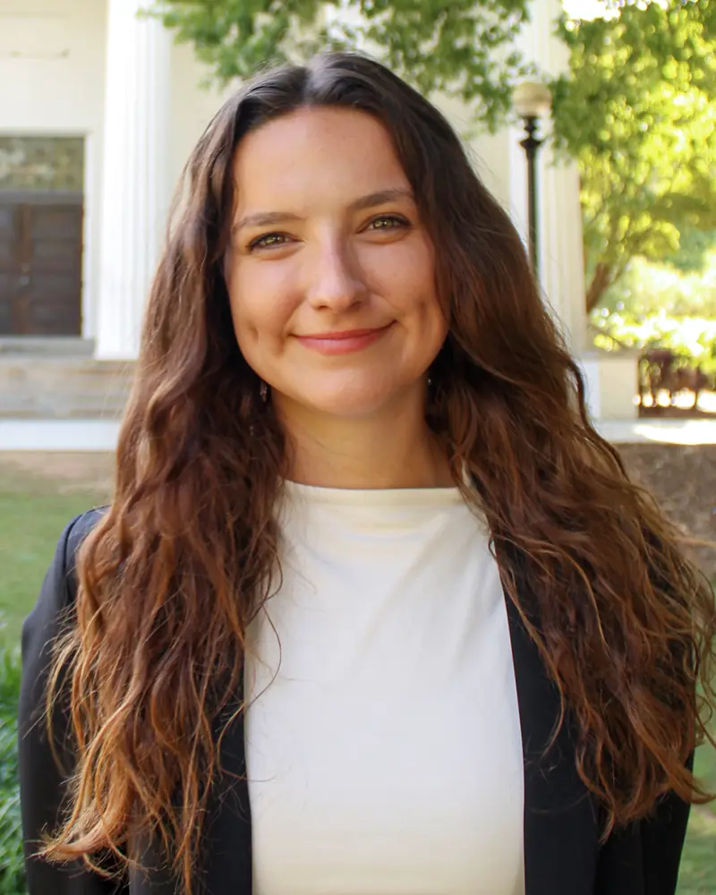 Headshot of Emma Gleason, outside with trees and columns in the background.