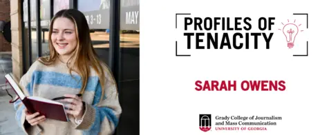 Sarah Owens smiles holding a red notebook and pen outside of a black glass building.